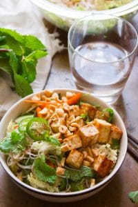 Bowl of Vietnamese Rice Noodle Salad with Hoisin Glazed Tofu with A Bunch of Mint and Drinking Glass in the Background