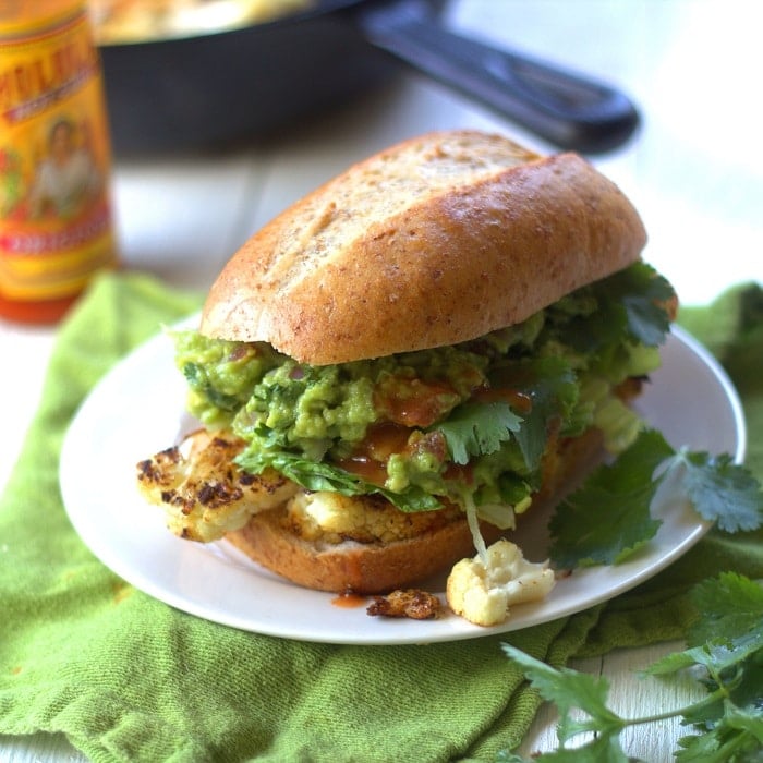 Cauliflower Steak and Guacamole Sandwich on a Plate with Bottle of Hot Sauce and Skillet in the Background