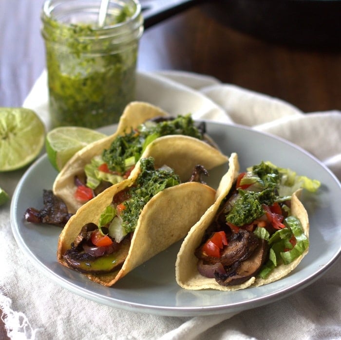 Three Portobello Tacos on a Plate with Jar of Chimichurri and Lime Slices in the Background