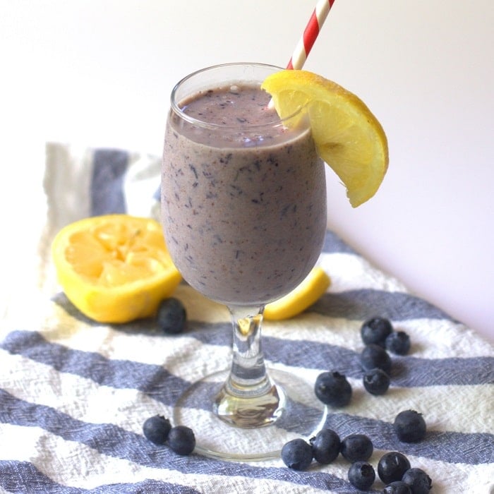 Glass of Blueberry Smoothie on a Striped Napkin with Lemon Wedges and Fresh Blueberries