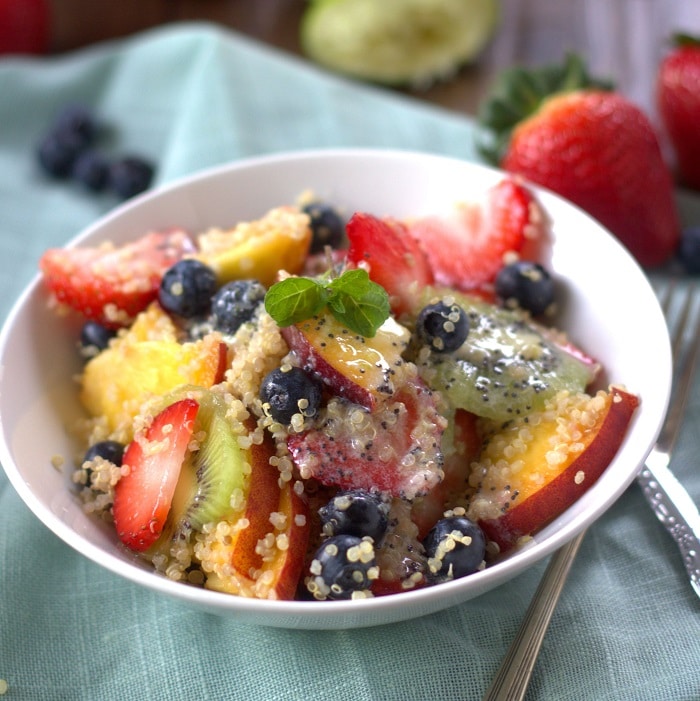 Bowl of Quinoa Fruit Salad with Berries in the Background and Silverware on the Side