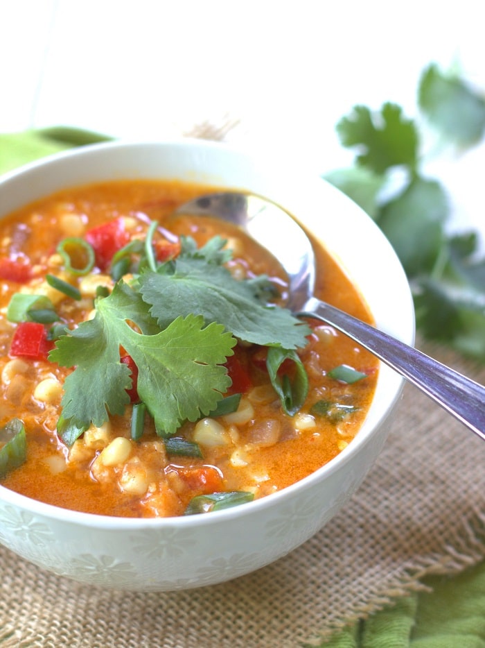 Close up of a bowl of red curry corn chowder with spoon.