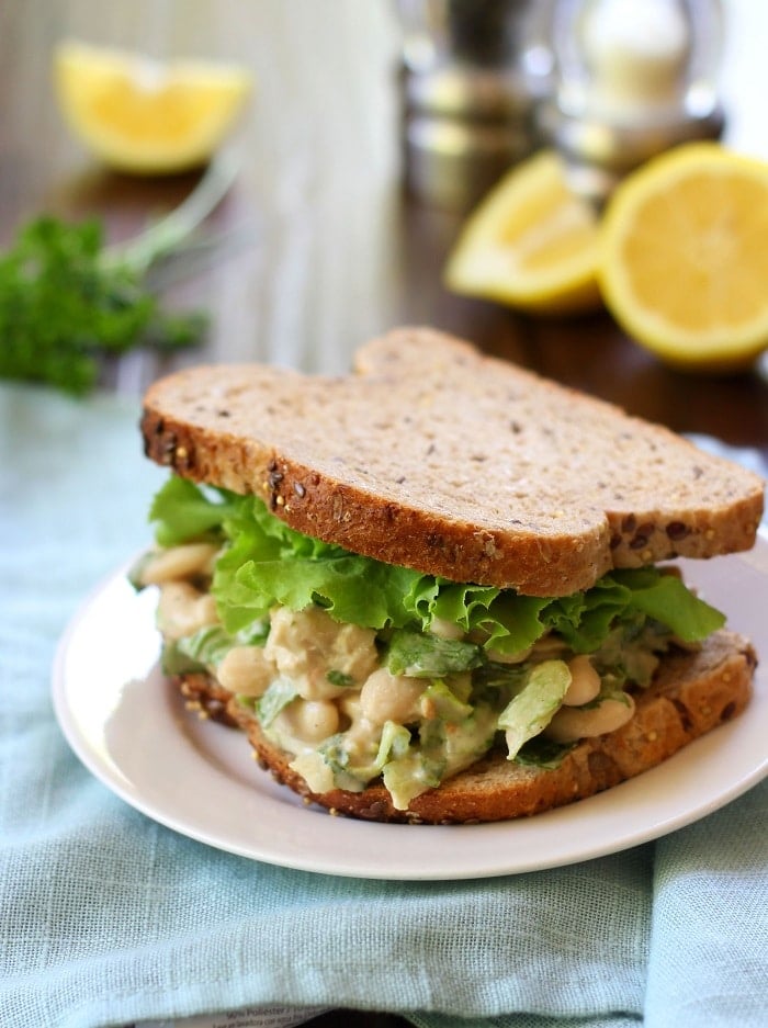 Vegan Caesar Salad Sandwich on a Plate with Lemon Wedges in the Background