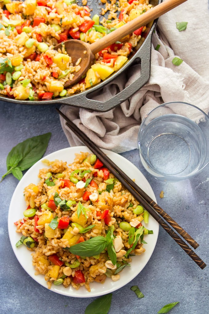 Pineapple Fried Rice on a Plate with Water Glass, Chopsticks and Skillet on a Blue Background