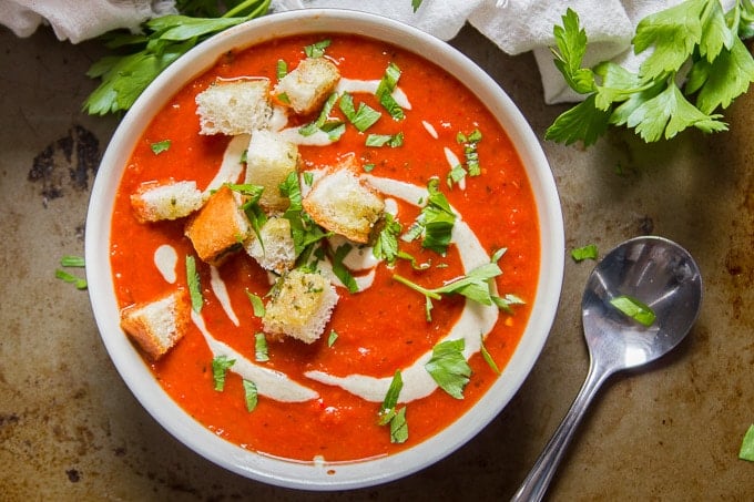 Overhead View of a Bowl of Roasted Red Pepper Soup with Garlic Bread Croutons with Spoon on the Side