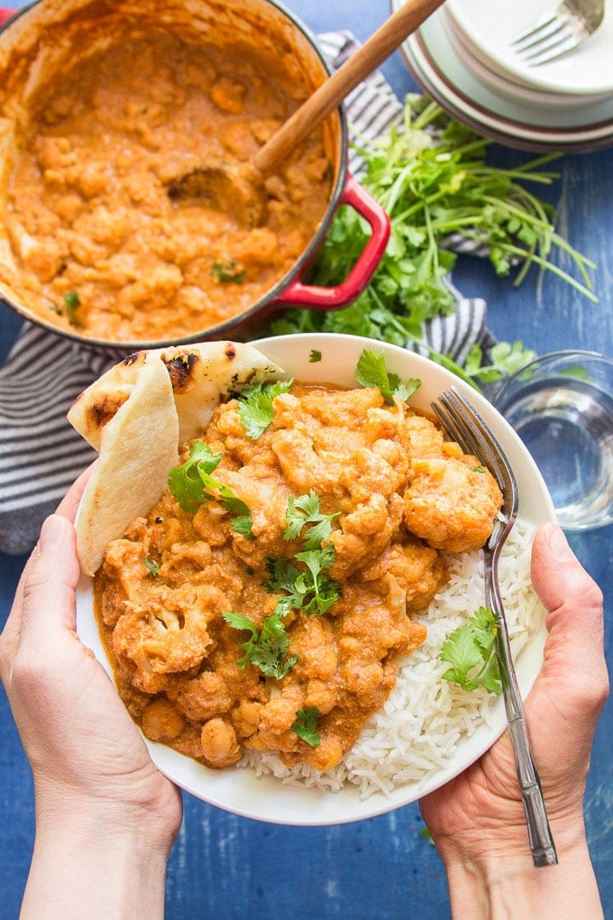 Hands Holding a Bowl of Vegan Tikka Masala Over a Table