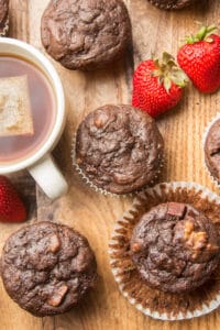 Vegan Chocolate Zucchini Muffins, a Cup of Tea, and Strawberries Arranged on a Wooden Surface