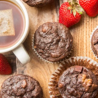 Vegan Chocolate Zucchini Muffins, a Cup of Tea, and Strawberries Arranged on a Wooden Surface