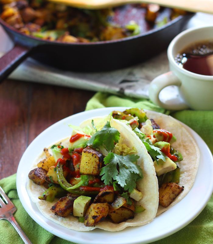 Two Curried Potato Tacos on a Plate with Tea Cup and Skillet in the Background