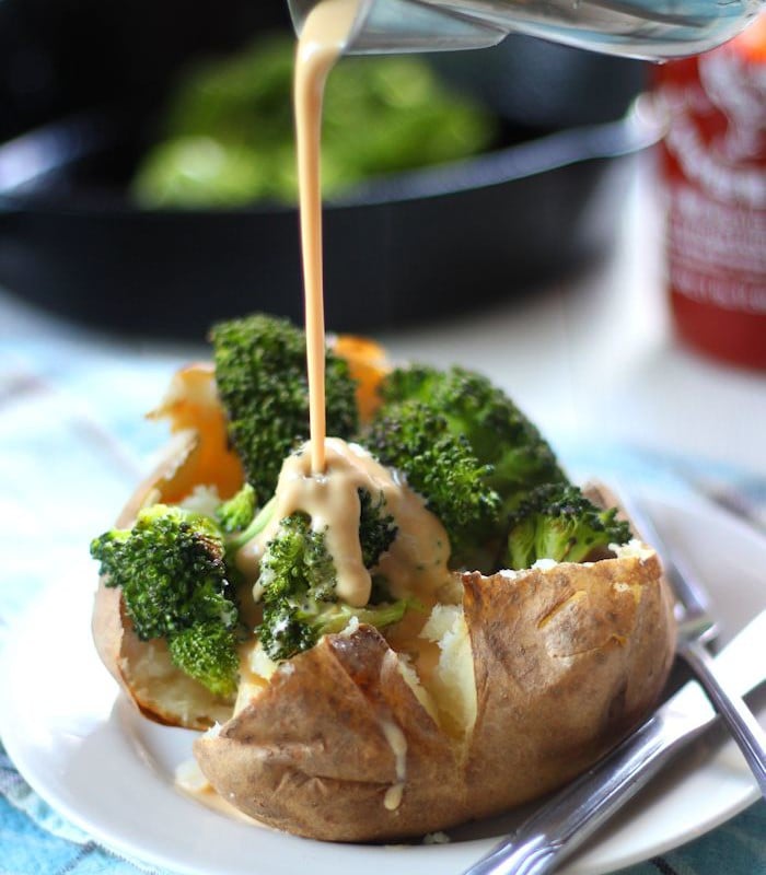 Vegan Cheese Sauce Being Drizzled Over a Broccoli Stuffed Potato