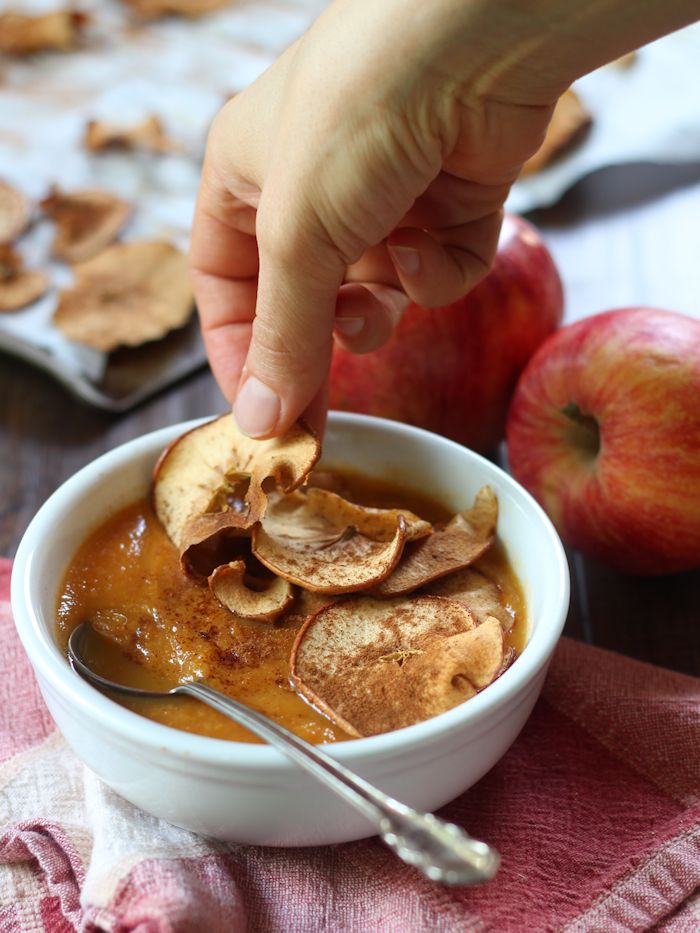 Hand Placing an Apple Chip on Top of a Bowl of Sweet Potato Soup