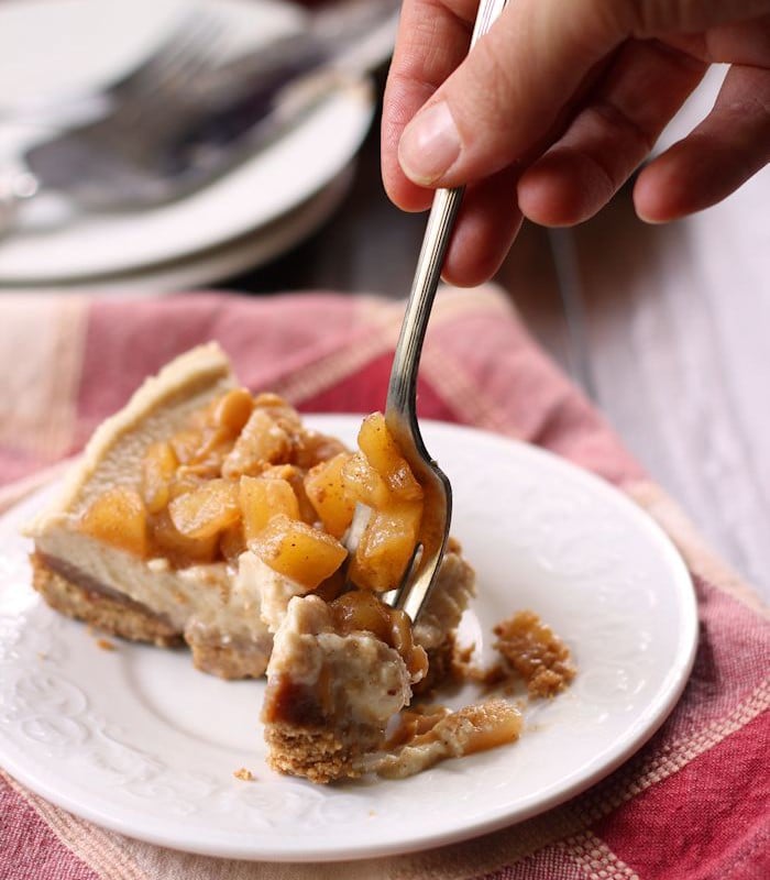 Hand with Fork Digging into a Slice of Vegan Caramel Apple Cheesecake on a Plate