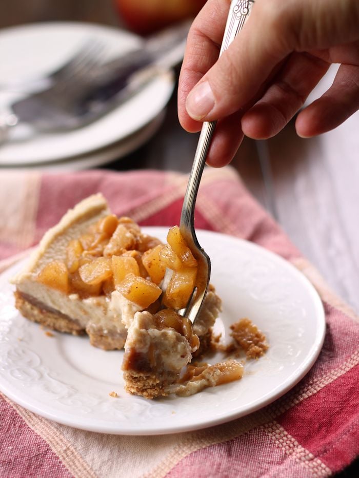 Hand with Fork Digging into a Slice of Vegan Caramel Apple Cheesecake on a Plate