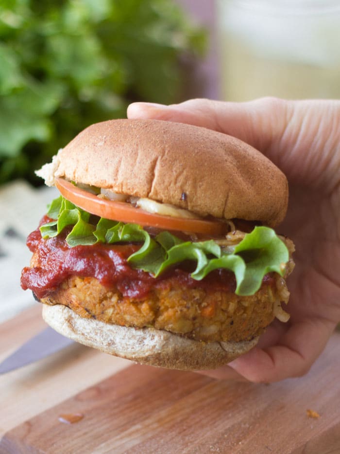 Hand Holding a Vegan Meatloaf Burger Topped with Lettuce, Tomato and Sauce