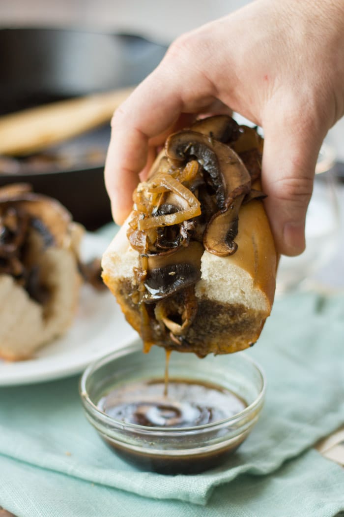 Vegan French Dip Sandwich Being Dipped into a Dish of Au Jus