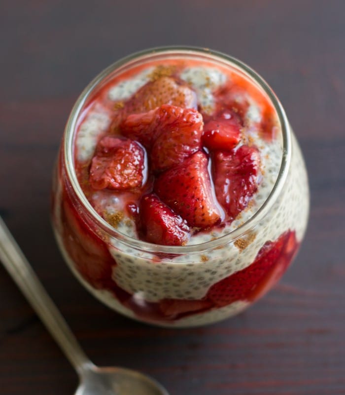 Jar Filled with Layers of Vanilla Chia Pudding and Roasted Strawberries Sitting on a Wooden Surface