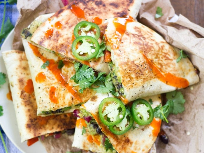 A Plate of Quartered Avocado Quesadillas Topped with Hot Sauce and Jalapeno Peppers