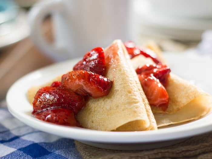 Vegan Crepes and Roasted Strawberries on a Plate with Coffee Cup in the Background
