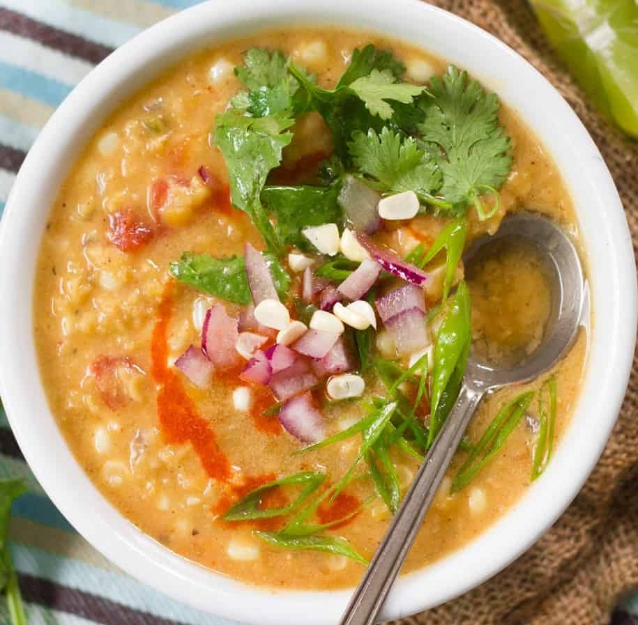 Bowl of red lentil corn chowder topped with red onion and cilantro.