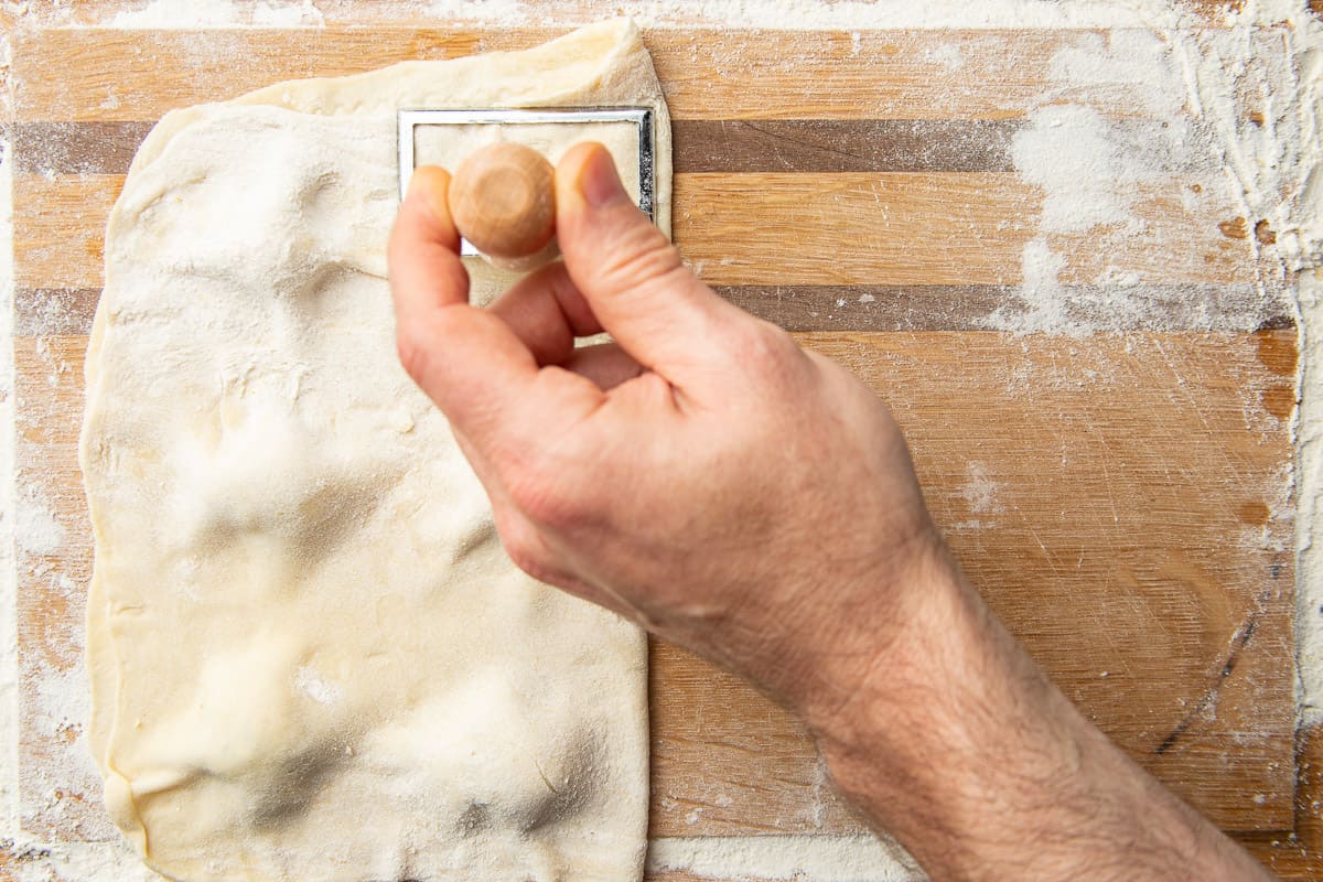 Hand cutting Vegan Ravioli in dough with a ravioli cutter.