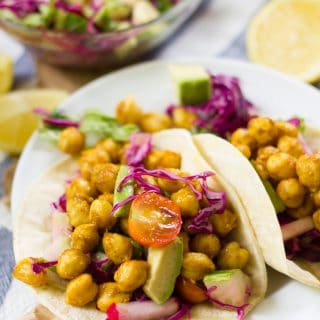 Two Curried Chickpea Tacos on a Plate, with Lemon Half and Salad Bowl in The Background