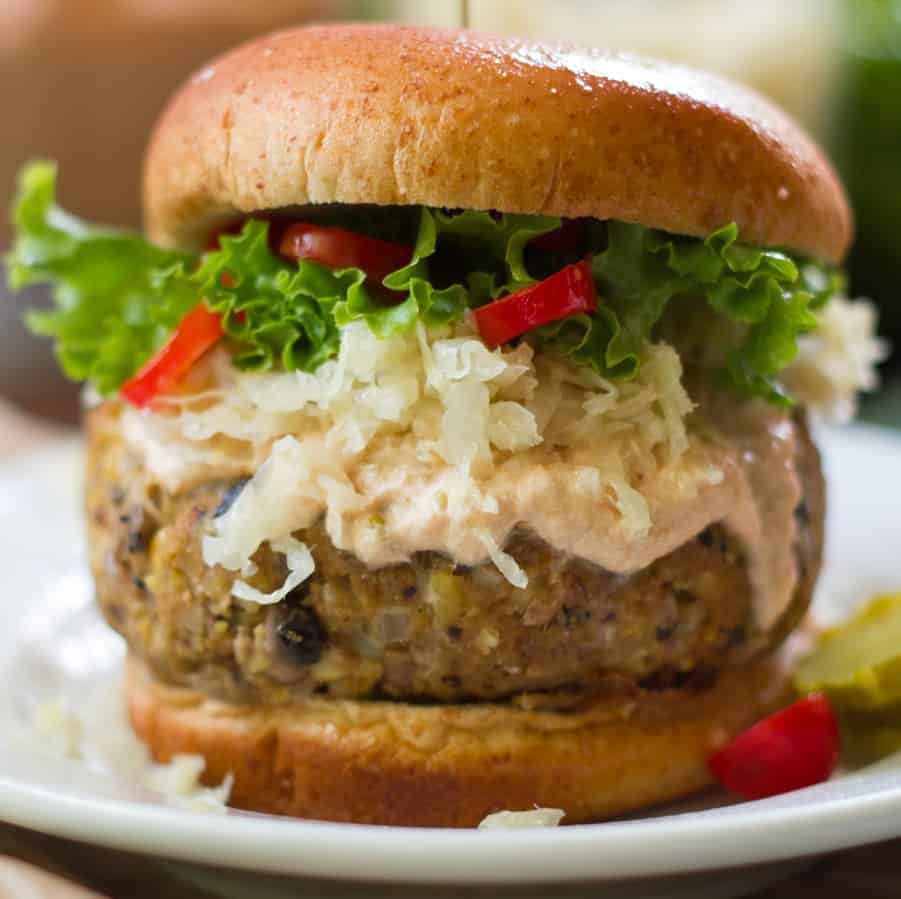 Close up of a vegan Reuben burger topped with dressing and saurerkaut.
