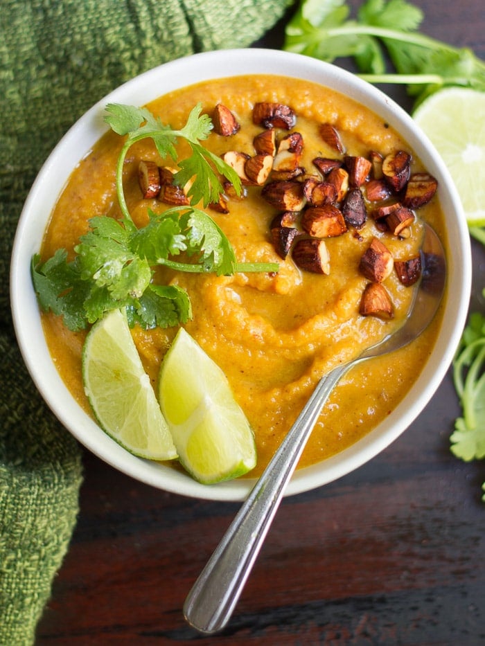 Overhead View of a Bowl of Thai Sweet Potato Carrot Soup Topped with Fresh Cilantro, Almonds, and Lime Wedges