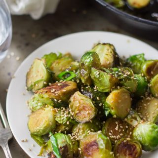 Sweet & Sour Brussels Sprouts Topped with Sesame Seeds on a Plate, Skillet in the Background