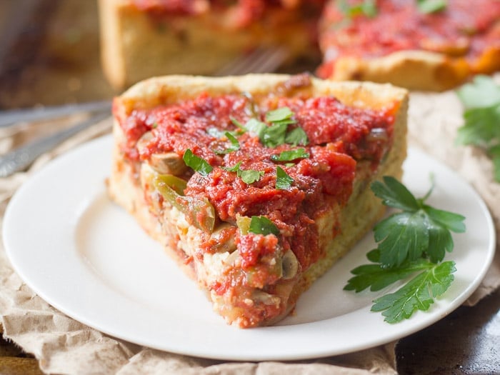 Close Up of a Slice of Vegan Deep Dish Pizza Pointed at the Viewer and Sitting on a Plate