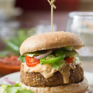 n Lentil Nacho Burger Topped with Tahini Cheese, Tomato Slices, Onions and Jalapenos on a Plate