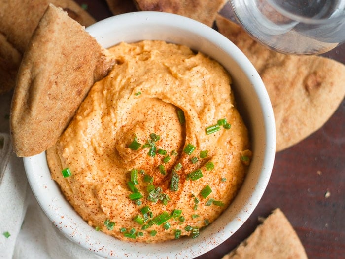 Overhead View of a Bowl of Buffalo Hummus Surrounded by Pita Bread and a Glass of Water
