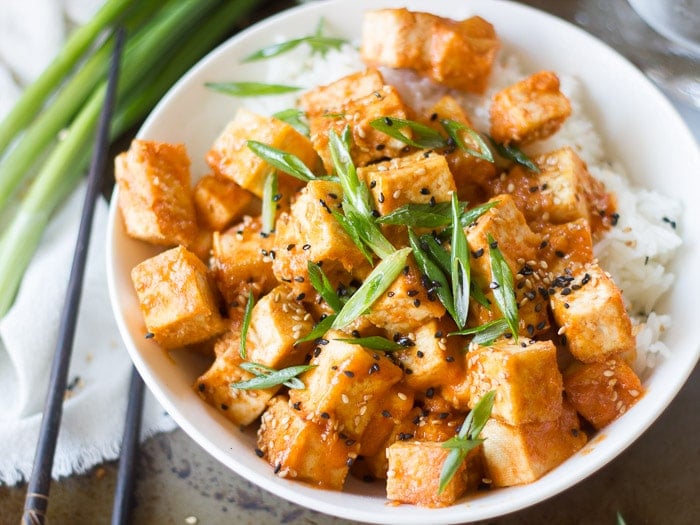 Close Up of a Bowl of Sesame Sriracha Tofu Topped with Sesame Seeds and Scallions