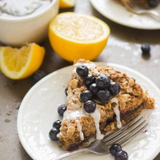 Slice of Vegan Lemon Blueberry Coffee Cake on a Plate with Tea Cup and Lemon Slices in the Background