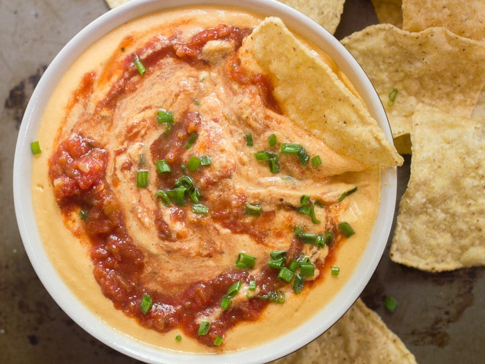 Overhead View of a Bowl of Nacho Cauliflower Cheese with Salsa and Chives on Top, Surrounded by Tortilla Chips