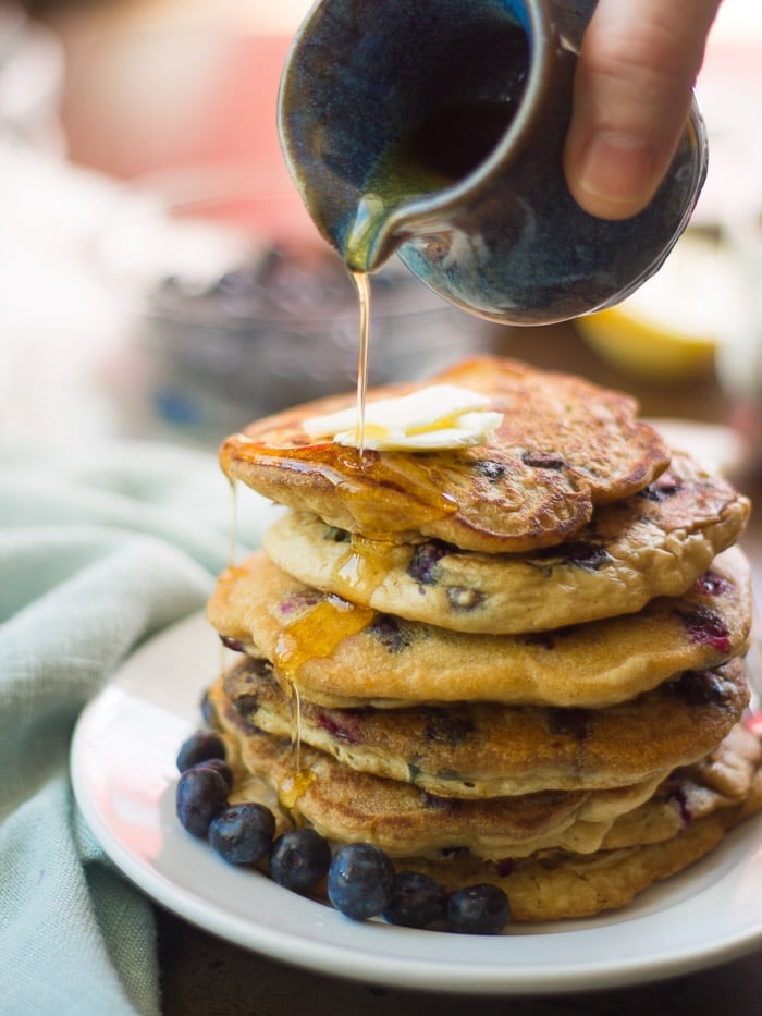 Hand Pouring Syrup Over a Stack of Vegan Blueberry Pancakes