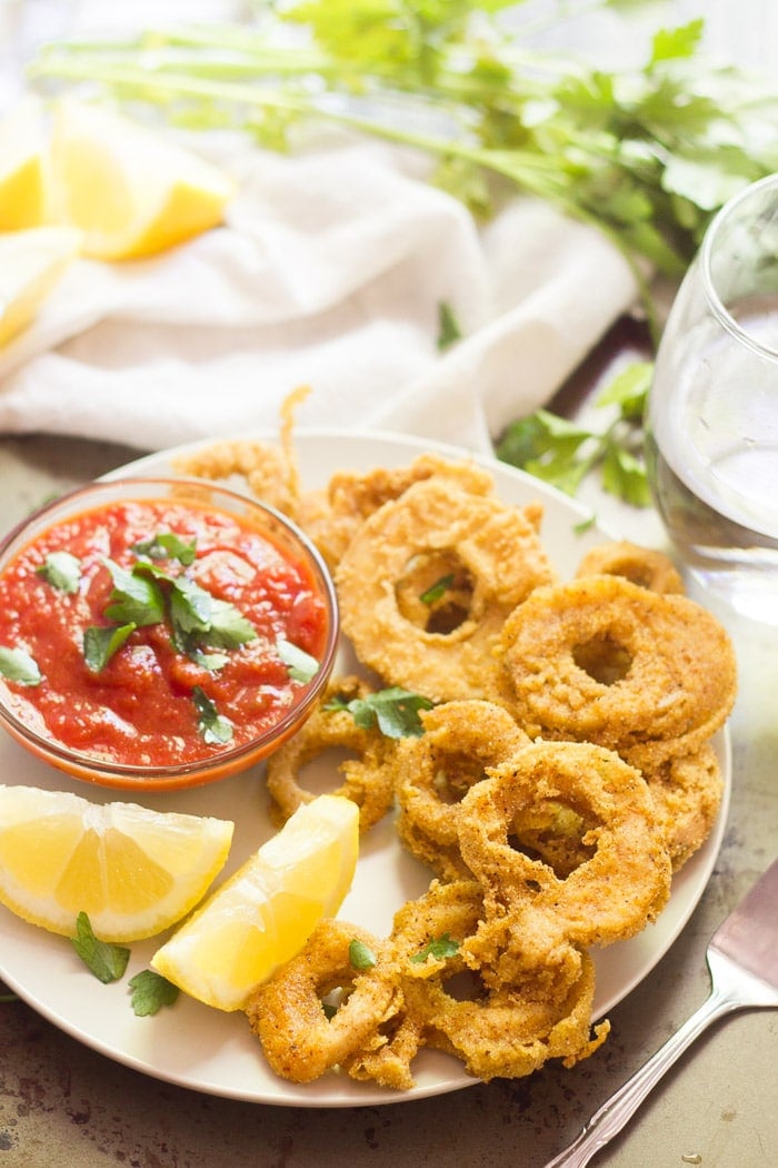 Trumpet Mushroom Calamari on a Plate with a Bowl of Marinara Sauce and Lemon Wedges, Drinking Glass and Fresh Parsley in the Background