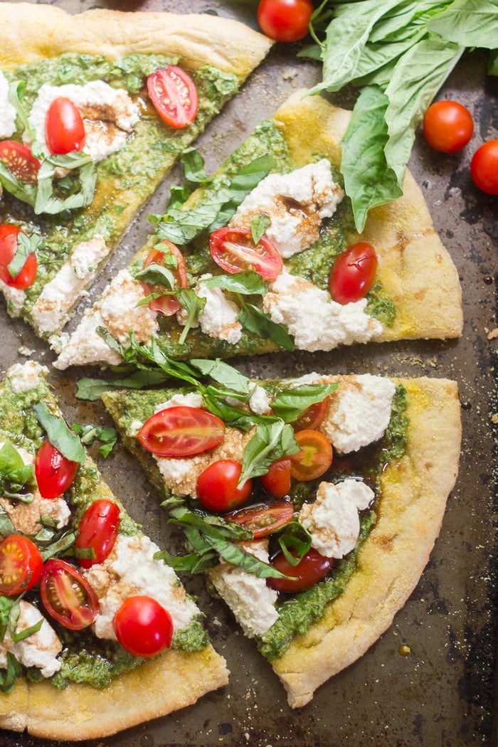 Slices of Vegan Pesto Caprese Pizza on a Baking Sheet with Cherry Tomatoes and Fresh Basil