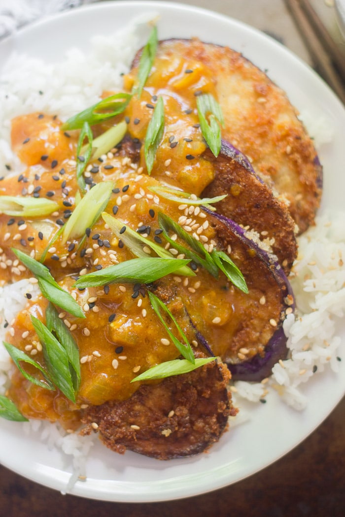 Katsu de berenjena al curry con semillas de sésamo y cebolletas en un plato sobre arroz