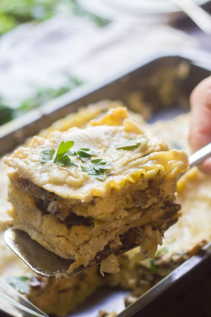 Slice of Creamy Vegan Mushroom Lasagna Held on a Server Over a Baking Dish