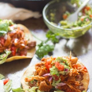 Two Jackfruit Tinga Tostadas with Skillet and Bowl of Guacamole in the Background
