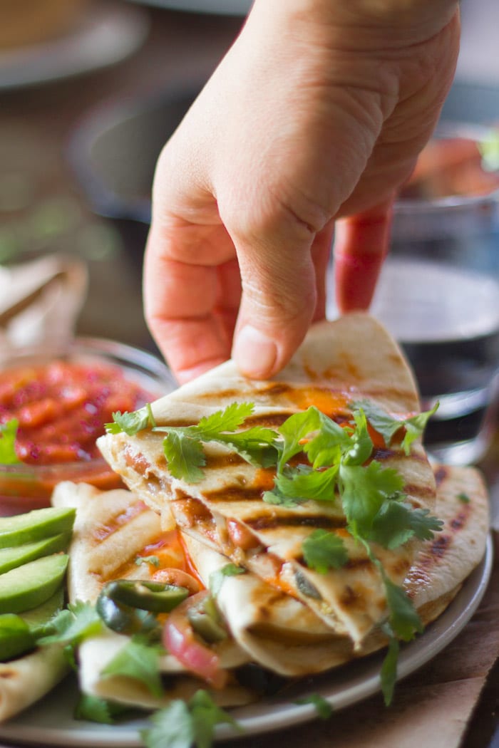 Hand Grabbing a Slice of a Vegan Quesadilla From a Plate