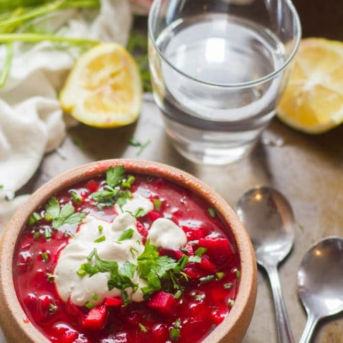 Bowl of Vegan Borscht with Lemon Slices and Water Glass in the Background