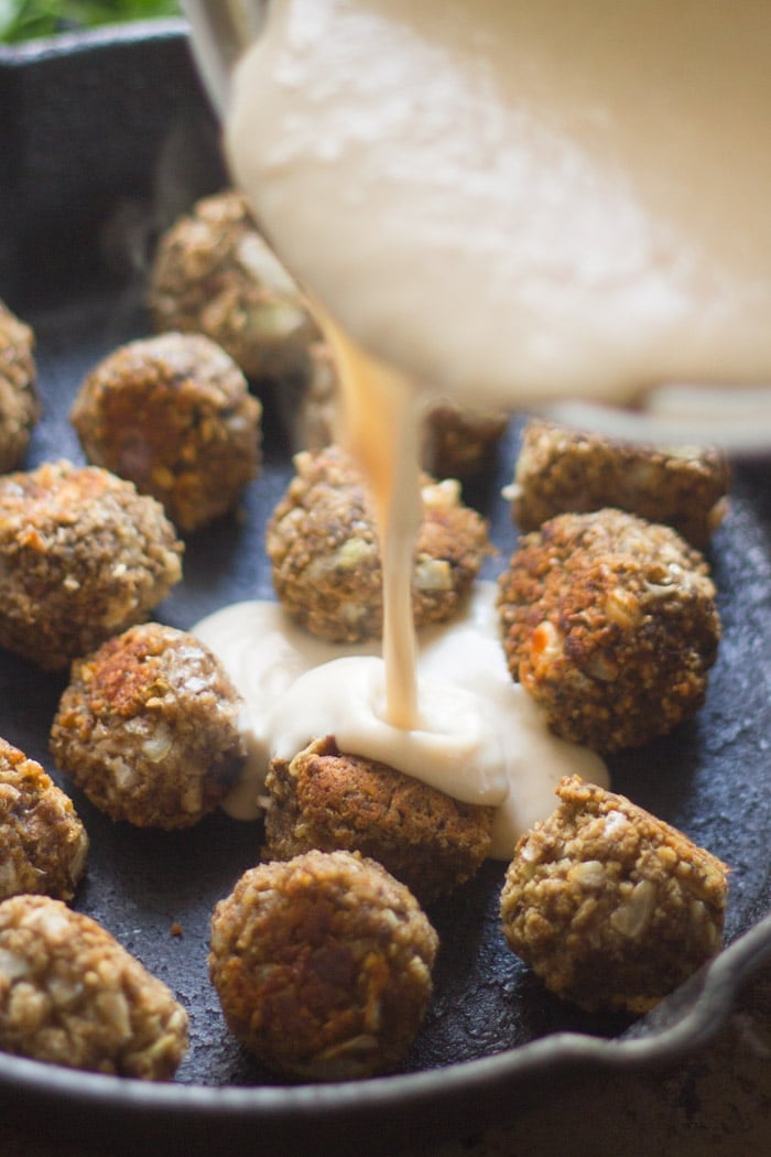 Vegan Swedish Meatballs in a Skillet with Cream Sauce Being Poured Over Them,
