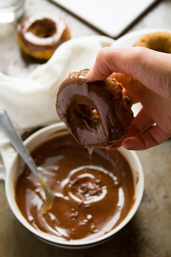 Hand Dipping a Banana Doughnut into a Bowl of Chocolate Peanut Butter Frosting