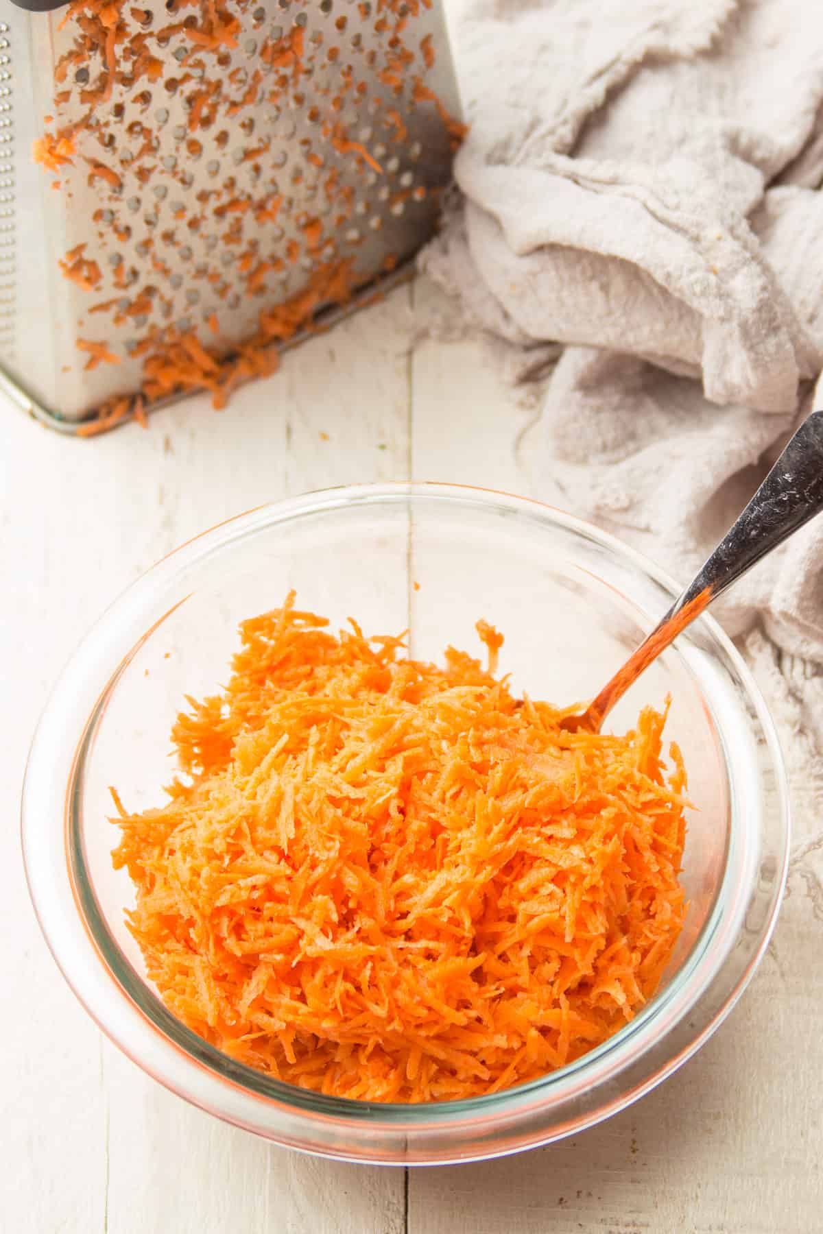 Bowl of Shredded Carrots with a Box Grater in the Background