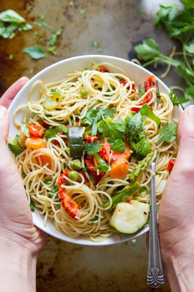 A Pair of Hands Holding a Bowl of Vegan Pasta Primavera