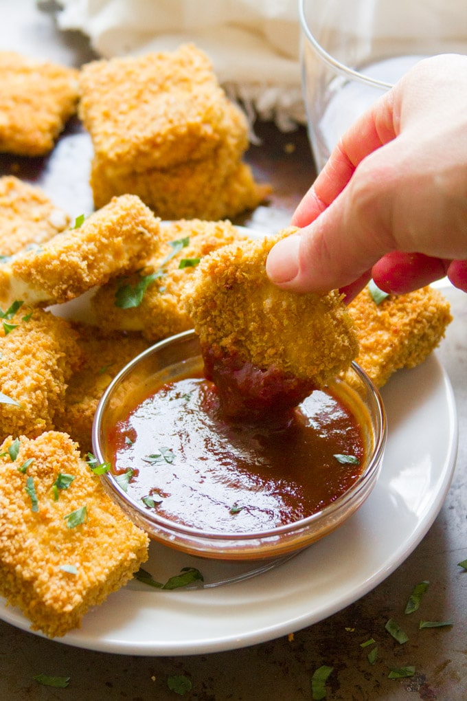 Hand Dipping a Crispy Baked Tofu Nugget Into a Bowl of Dipping Sauce