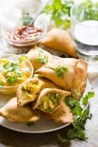 Plate of Baked Vegan Samosas with Dishes of Chutney and Water Glass in the Background