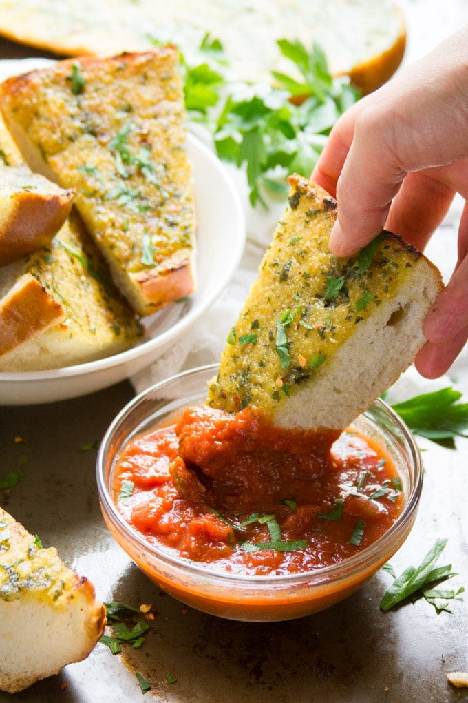 Hand Dipping a Slice of Roasted Garlic Vegan Garlic Bread in Tomato Sauce