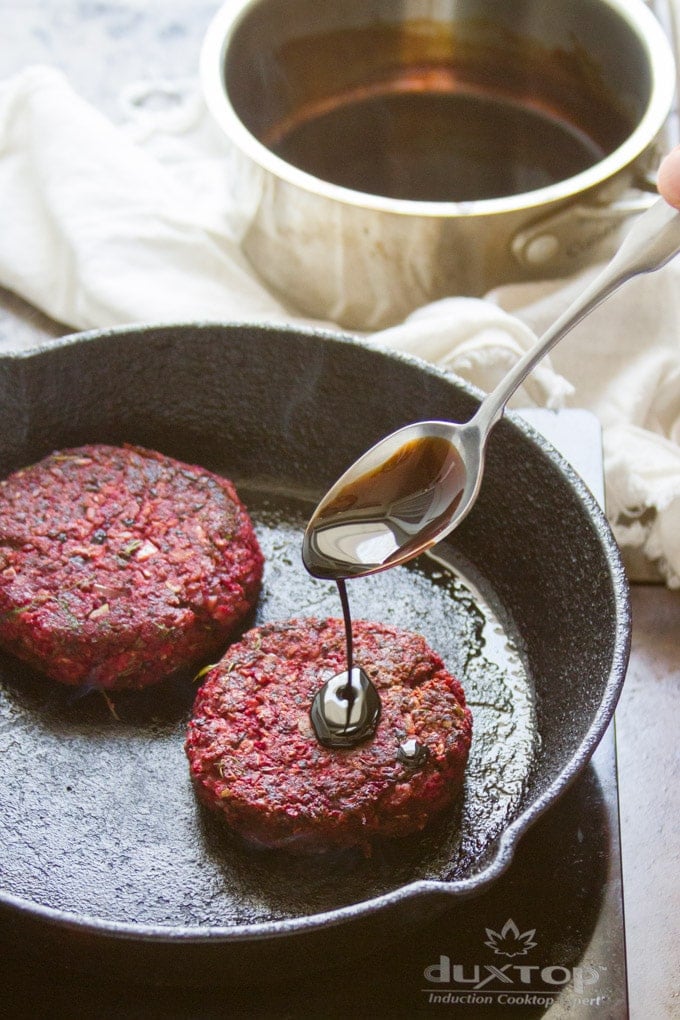 Spoon Drizzling Balsamic Vinegar Over Beet Burger Patties in a Skillet